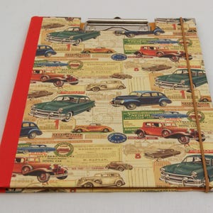 May include: A red and brown clipboard with a vintage car pattern. The clipboard has a metal clip and a brown elastic band.
