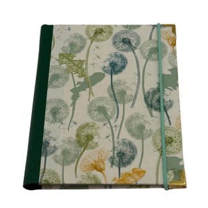 Peut inclure: Un carnet rectangulaire avec une couverture crème ornée d'un motif botanique de pissenlits et de feuilles dans des tons de vert, bleu et jaune. Il possède un dos vert foncé, un élastique de fermeture vert clair et des coins en métal doré.