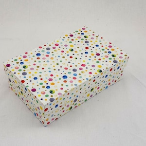 Könnte beinhalten: Eine rechteckige Aufbewahrungsbox mit weißem Untergrund, die mit einem verstreuten Muster aus bunten, aquarellartigen Punkten in verschiedenen Größen bedruckt ist. Der Deckel passt auf die Box und das Design bedeckt Deckel und Seiten.