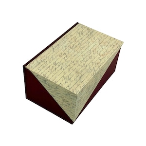 Könnte beinhalten: Eine rechteckige Aufbewahrungsbox mit einer tiefroten Basis und einem Deckel, der mit einem cremefarbenen Papier im Vintage-Stil überzogen ist. Die Deckeloberfläche ist mit dichter, dunkelbrauner Schreibschrift bedruckt, die historisch wirkt.