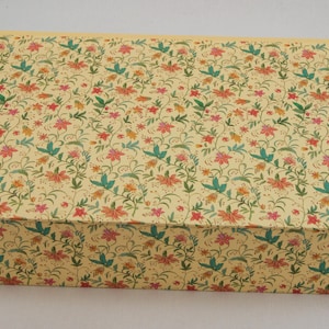 Könnte beinhalten: Eine rechteckige Aufbewahrungsbox mit cremefarbenem Hintergrund und einem wiederkehrenden Muster aus kleinen roten und orangefarbenen Blumen mit grünen Blättern und dünnen, gewundenen Stielen. Die Box hat einen flachen Deckel und eine kantige Form.