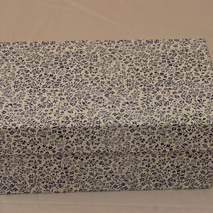 Könnte beinhalten: Rechteckige Schachtel mit Deckel, bedeckt mit weißem Stoff mit einem sich wiederholenden Muster aus kleinen, dunkelblauen Blumen- und Blattdesigns. Ideal für die Aufbewahrung oder als Geschenkbox.