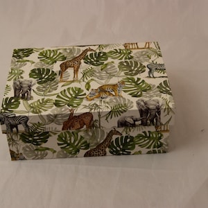 Peut inclure: Une boîte de rangement rectangulaire à fond blanc ornée d'un motif répétitif de feuilles de monstera vertes et d'animaux sauvages tels que des girafes, des éléphants, des tigres et des zèbres. La boîte possède un couvercle amovible assorti.