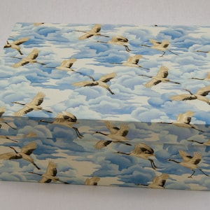 Könnte beinhalten: Eine rechteckige Aufbewahrungsbox mit einem sich wiederholenden Muster aus weißen Kranichen im Flug vor einem Hintergrund aus hellblauen und weißen Wolken. Das Design bedeckt sowohl den Deckel als auch die Seiten der Box.