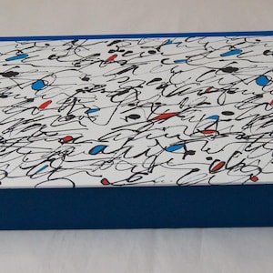 Puede incluir: Caja rectangular con tapa blanca con un diseño abstracto de garabatos en negro, azul y rojo. La caja tiene una base azul sólida y un borde azul a juego. Ideal para almacenamiento o como caja de regalo.