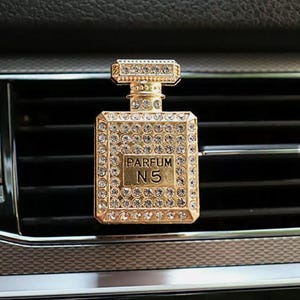 May include: Gold car air freshener shaped like a perfume bottle with rhinestones and the text "PARFUM N5".