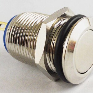 May include: A chrome push button switch with a silver button face and a black rubber seal. The switch has a ridged body and a blue base with a gold terminal.