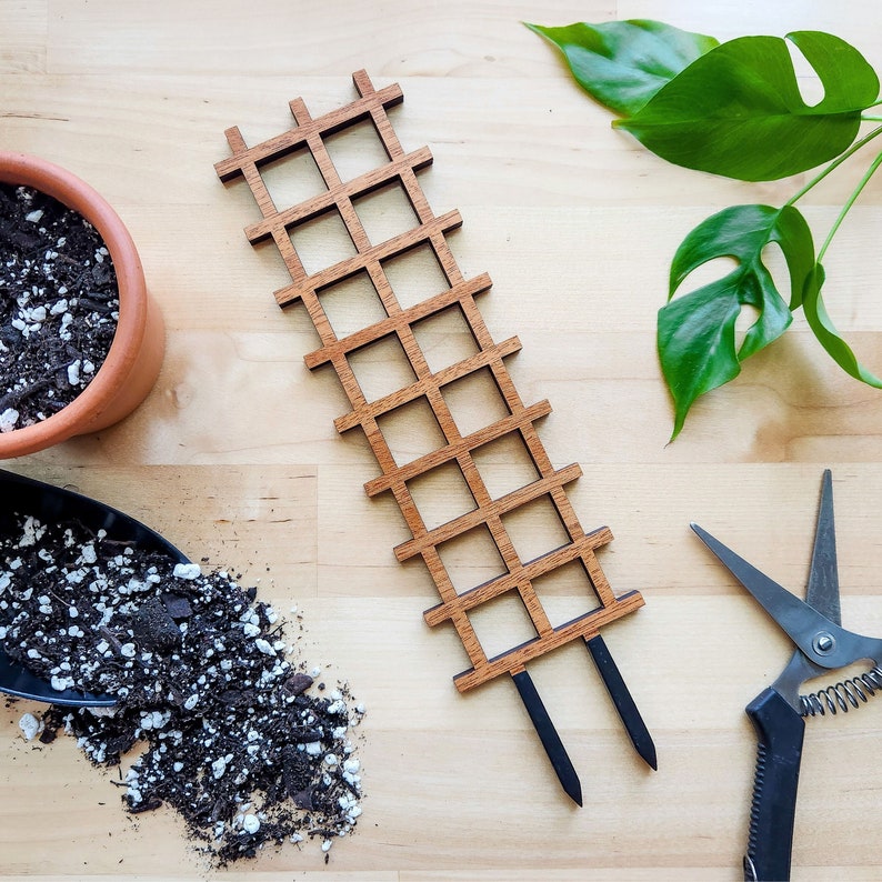 May include: A wooden trellis with a grid pattern, perfect for supporting climbing plants. The trellis has two stakes for easy insertion into the ground.