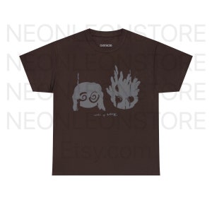 May include: A brown t-shirt featuring a gray graphic design. The design includes two stylized figures and the text "wake up LOCKI" in a handwritten font. The shirt has a classic crew neck and short sleeves.