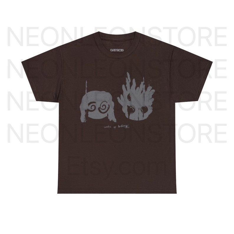 May include: A brown t-shirt featuring a gray graphic design. The design includes two stylized figures and the text "wake up LOCKI" in a handwritten font. The shirt has a classic crew neck and short sleeves.