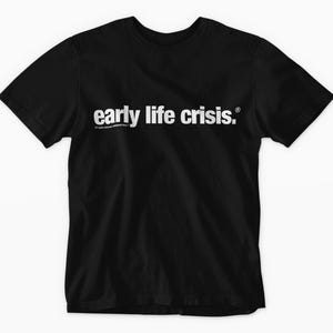 May include: Black t-shirt with the phrase "early life crisis" in white, centered on the chest. The text is in a bold, sans-serif font. Below the main text is smaller text. The shirt has short sleeves and a crew neck.