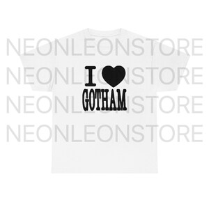 May include: White t-shirt with the phrase "I &hearts; GOTHAM" printed in black. The heart symbol is solid black. The shirt is a classic crew neck style.