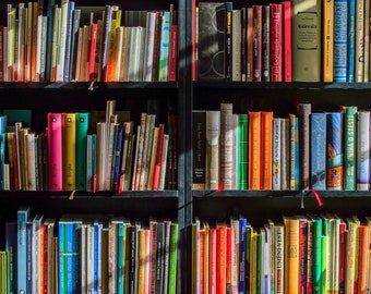 May include: A full bookshelf with rows of colorful books. The spines display a variety of colors, including pink, green, yellow, and blue. Some books have text visible, such as "Kalevala" and "Kniha o Stesti".