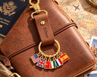 May include: A brown leather keychain with a gold-tone metal lobster clasp and ring. The leather strap is engraved with the name Ethan. Attached to the gold ring are six small square charms featuring the flags of the USA, UK, China, Italy, France, and Spain.