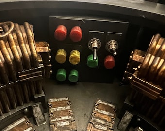 May include: A close-up of a control panel with red, yellow, and green buttons, and two silver toggle switches. The panel is surrounded by a metallic structure with copper-colored pipes.