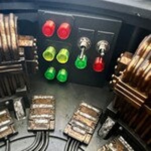 May include: Close-up of a control panel with red, green, and yellow buttons and switches. The panel is made of black plastic and has a metallic finish.