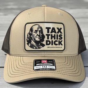 Może przedstawiać: Beżowo-czarna czapka typu trucker z naszywką przedstawiającą Benjamina Franklina i napisem "TAX THIS DICK". Czapka jest regulowana i posiada metkę Richardson 112.