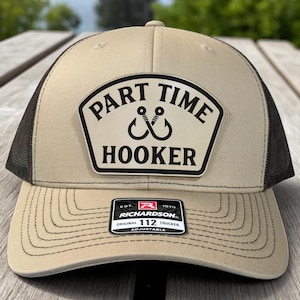 Może przedstawiać: Beżowo-czarna czapka typu trucker z czarnym napisem "PART TIME HOOKER" na białej naszywce. Czapka ma zakrzywiony daszek i siatkową tylną część. Widoczna jest etykieta marki Richardson.