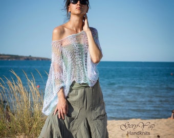 May include: A woman wearing a light blue crochet top and a long, olive green skirt. She is standing on a sandy beach with tall grass in the foreground and the ocean in the background. The text "Gery Yap Handknits" is visible in the lower right corner of the image.