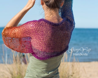 May include: A woman wearing a multi-colored crochet top with a gradient of orange, purple, and blue. The top is a loose, open-weave design. The woman is standing on a sandy beach with the ocean in the background. The text "Gery Yap Handknits" is visible in the lower right corner of the image.
