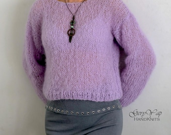 May include: A light purple fuzzy knit sweater with a scoop neck and long sleeves. The sweater is worn by a person with a necklace and a gray skirt.