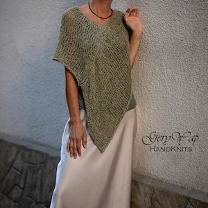 Può includere: Un poncho verde lavorato a maglia con scollo a V. Il poncho è abbinato a una gonna lunga colorata. L'immagine include anche occhiali da sole e una collana. Il testo "Gery Yap HANDKNITS" è visibile.