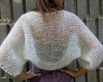 May include: White knitted shrug with a delicate openwork pattern. The shrug is lightweight and sheer, perfect for layering.