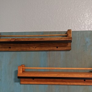 May include: Two wooden shelves with black metal rails mounted on a blue wall. The shelves are stained a dark brown color.