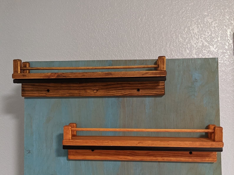 May include: Two wooden shelves with black metal rails mounted on a blue wall. The shelves are stained a dark brown color.