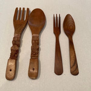 May include: A set of four brown wooden utensils consisting of two large forks and spoons with carved totem-style handles, alongside two smaller, smooth-handled forks and spoons. Each piece features a polished finish and distinct wood grain patterns.