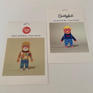 Pode incluir: Dois kits de modelos de papel ChattyFeet. O kit da esquerda é o Henri Fold-Kiss, com uma figura de barba branca, óculos e camisa estampada. O kit da direita é o David Fold-Me, com uma figura de cabelo loiro, óculos vermelhos e camisa azul.