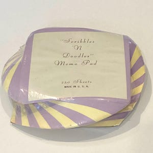 May include: A round memo pad with a purple and yellow striped pattern. The center label reads "Scribbles 'N Doodles" Memo Pad, 250 Sheets, MADE IN U. S. A. The pad is wrapped in clear plastic and features a stack of paper sheets.