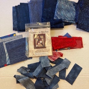 Pode incluir: Uma coleção de retalhos de tecido em tons de azul e vermelho, incluindo peças estampadas e lisas. Um saco plástico transparente contém um livreto de padrões intitulado Seasons in Patches, Summer, An Art Hanging for Every Season.