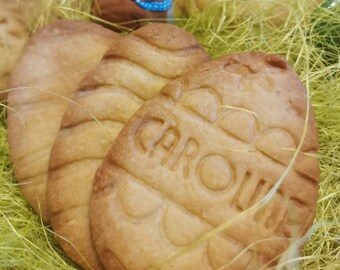 May include: Close-up of three Easter-themed sugar cookies. Two cookies are decorated with a wavy pattern, and one cookie is decorated with the word "CAROLE" in a cursive font.