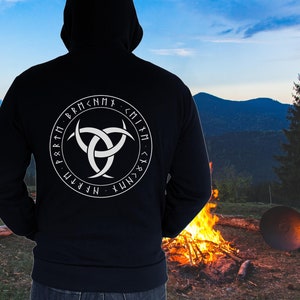 Könnte beinhalten: Ein schwarzer Kapuzenpullover mit einem weißen Symbol und Runen auf der Rückseite. Das Symbol ist ein Triquetra, ein dreispitziger Knoten, umgeben von einem Kreis aus Runen. Die Runen sind kreisförmig angeordnet und buchstabieren "NFRTM P Q R 1 M ;RM <NMX・MM <1 & <N MY".