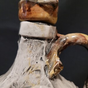 Op de afbeelding: Een keramische kan met een witte glazuur en bruine accenten. De kan heeft een uniek, getextureerd oppervlak en een brede, afgeronde opening. De bovenkant van de kan is bedekt met een bruin deksel.