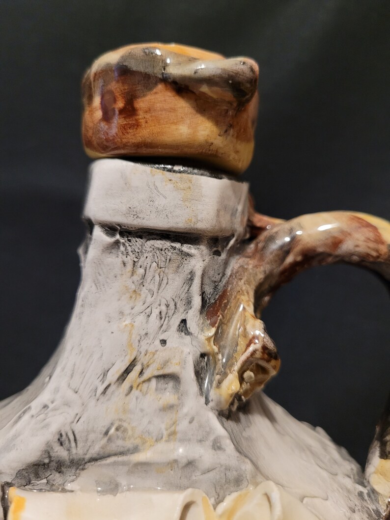 Op de afbeelding: Een keramische kan met een witte glazuur en bruine accenten. De kan heeft een uniek, getextureerd oppervlak en een brede, afgeronde opening. De bovenkant van de kan is bedekt met een bruin deksel.