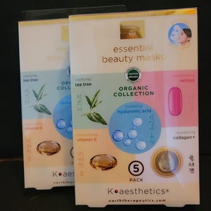 Puede incluir: Dos cajas de mascarillas de belleza esenciales Koaesthetics. Cada caja presenta texto que indica árbol de té clarificante, vitamina E hidratante, ácido hialurónico hidratante y colágeno revitalizante. Las cajas son blancas con detalles en azul, verde y dorado.