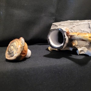 Op de afbeelding: Een keramische flessenstop met een boomschorsontwerp. De stop is gevormd als een boomstam met een ronde bovenkant en een gat in het midden. De stop is lichtbruin van kleur met donkerbruine accenten.