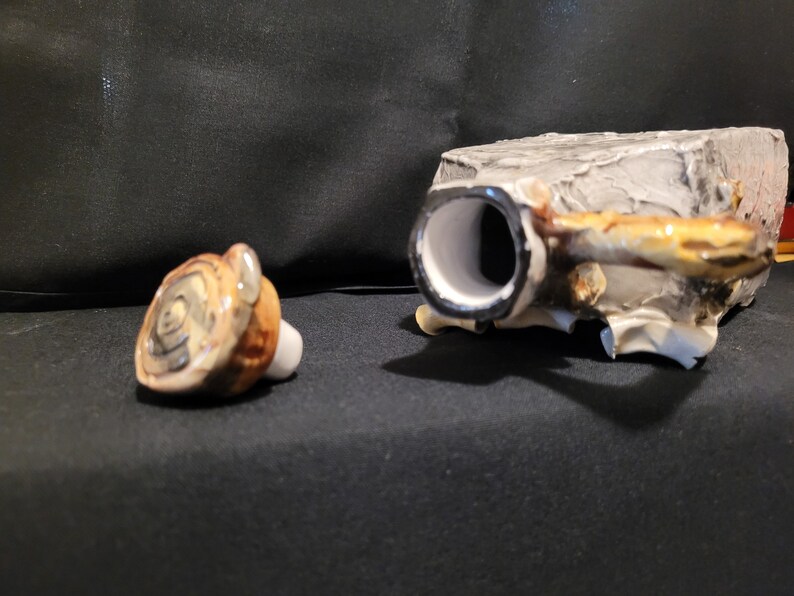 Op de afbeelding: Een keramische flessenstop met een boomschorsontwerp. De stop is gevormd als een boomstam met een ronde bovenkant en een gat in het midden. De stop is lichtbruin van kleur met donkerbruine accenten.