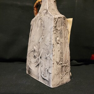 Op de afbeelding: Een witte keramische kan met een getextureerd oppervlak en een bruine handgreep. De kan heeft een uniek, abstract ontwerp.