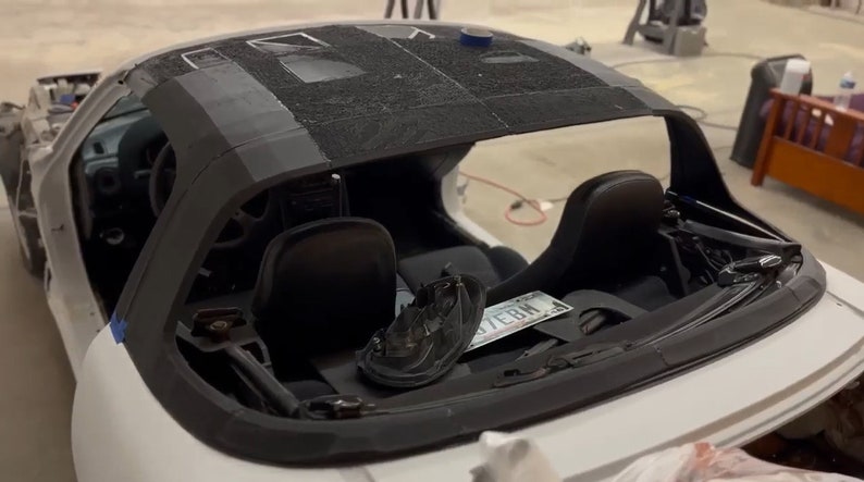 Op de afbeelding: Een witte cabriolet met zichtbaar interieur. De auto heeft zwarte stoelen en een zwart stoffen dak. De auto staat in een garage en heeft een kentekenplaat met de tekst "7EBM".