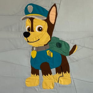 Puede incluir: Diseño de patchwork colorido de Chase de Paw Patrol. El personaje está representado con un uniforme de policía con gorra azul, camisa y mochila verde. La cara del perro es amarilla y marrón, con una nariz negra y una expresión sonriente.