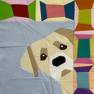 May include: A fabric quilt block featuring a geometric, pieced design of a light-colored dog with brown eyes and a black nose, set against a light blue background. The border consists of colorful, rectangular fabric segments in various hues.