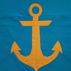 May include: A fabric quilt block featuring a golden yellow anchor centred on a solid teal background. The anchor is constructed using foundation paper piecing techniques with visible straight seams and stitching lines throughout the design.
