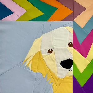 May include: A fabric quilt block featuring a geometric, pieced design of a golden-colored dog head against a light blue background. The dog has brown eyes and a black nose. The border consists of a vibrant, multi-colored chevron pattern.