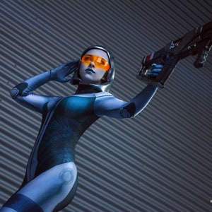 May include: A person in a futuristic blue and black bodysuit with orange-tinted goggles and a silver helmet, holding a black and grey weapon. The image is set against a corrugated metal background. The text "EDI03" and "star nacho cosplay" are visible.