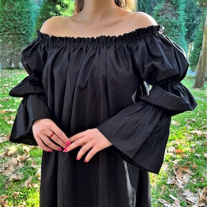 May include: A black off-the-shoulder dress with long, bell sleeves. The dress has a gathered neckline and a loose, flowing silhouette.