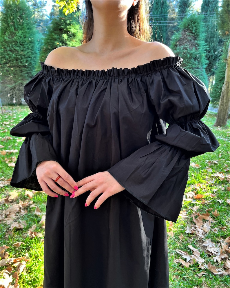 May include: A black off-the-shoulder dress with long, bell sleeves. The dress has a gathered neckline and a loose, flowing silhouette.