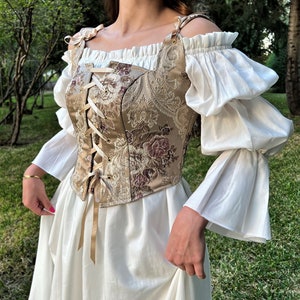 May include: A white off-the-shoulder peasant top with puffed sleeves and a brown and gold brocade corset with a lace-up front.